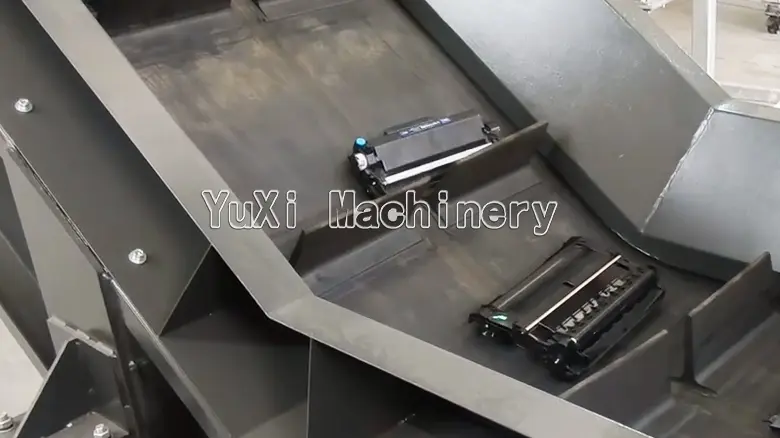 Waste ink cartridges being conveyed into the recycling machine hopper.