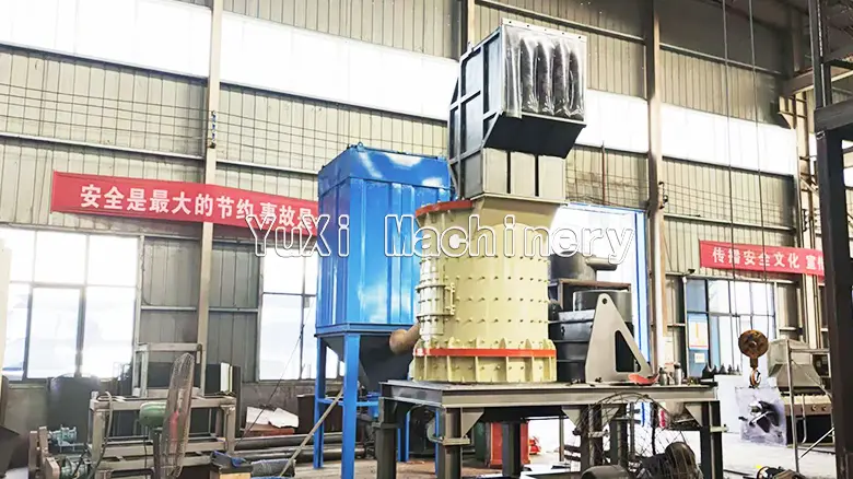 Large vertical shaft crusher installed in a workshop, connected to a blue dust collection or air separation unit.