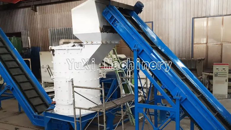 Vertical metal crusher connected to an inclined blue conveyor belt system for material feeding.